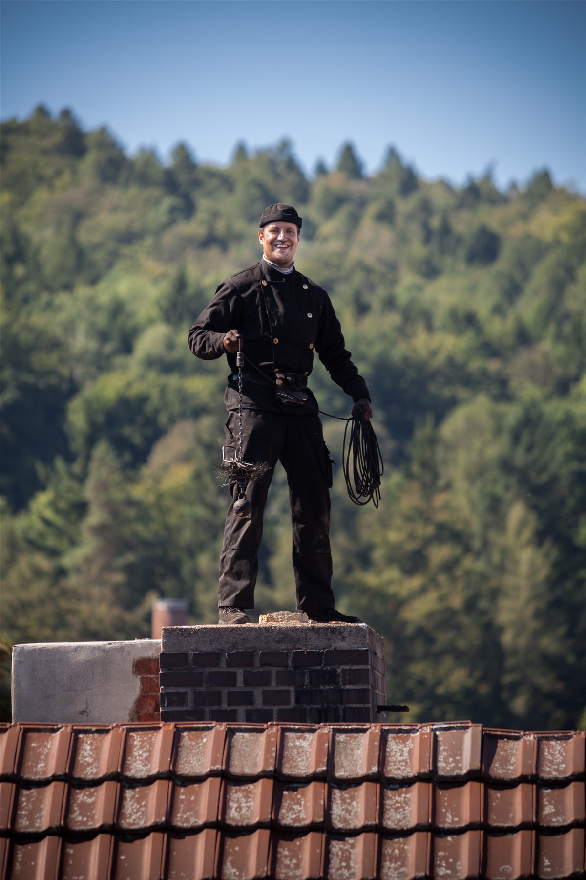 Real professional chimney sweep technician working on rooftop with chimney brush and brick chimney